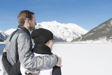 Austria, Tyrol, Achensee, couple looking at frozen lake in winter - MKFF00454