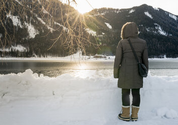 Austria, Tyrol, Achensee, woman standing at lake in winter at sunset - MKFF00464