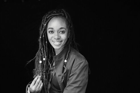 Porträt einer lächelnden Frau mit Dreadlocks vor einem schwarzen Hintergrund - FMKF05518