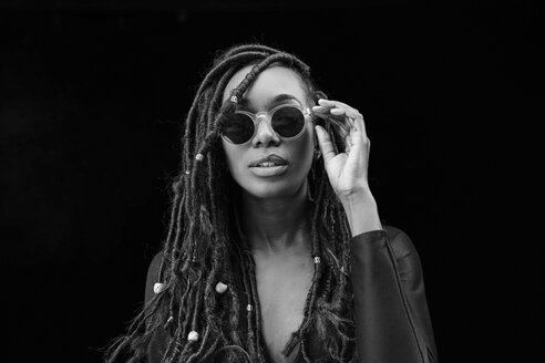 Portrait of woman with dreadlocks wearing sunglasses in front of black background - FMKF05525