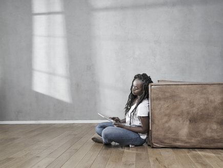 Frau sitzt auf dem Boden und benutzt ein digitales Tablet - FMKF05530