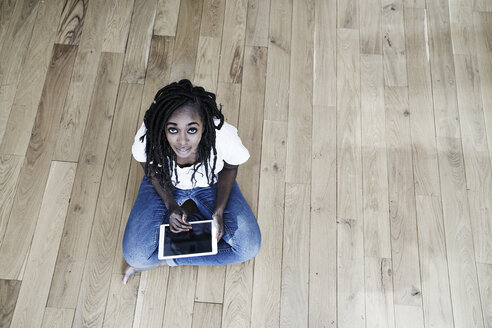 Porträt einer lächelnden Frau, die mit einem digitalen Tablet auf dem Boden sitzt - FMKF05533