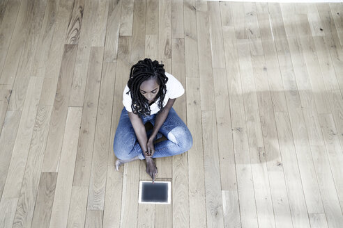 Frau sitzt auf dem Boden und benutzt ein digitales Tablet - FMKF05534
