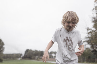 Portrait of blond boy with dirty face and t-shirt after jumping into a puddle - EYAF00021