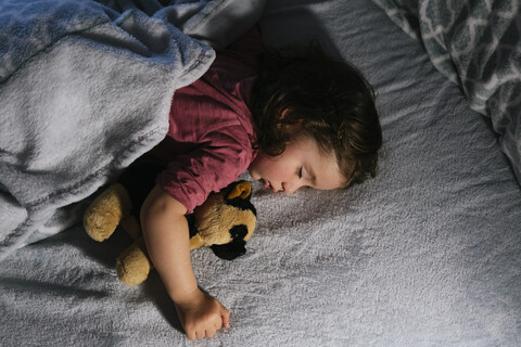 Mädchen im Kleinkindalter schläft im Bett mit einem Stofftierhund, lizenzfreies Stockfoto