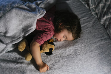 Toddler girl sleeping in bed with a soft toy dog - GEMF02911