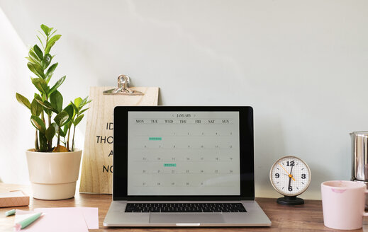 Opened laptop with a calendar on desk at home office - MOMF00633