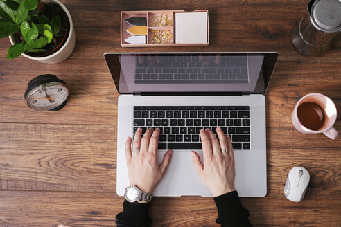 Woman's hands working on laptop at home office, top view - MOMF00639