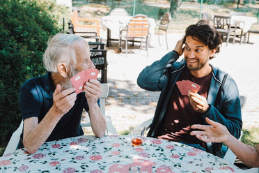 Smiling male caretaker playing cards with senior man and woman at table in back yard - MASF11529