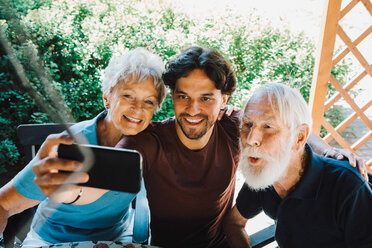 Smiling male caretaker taking selfie with senior man and woman at back yard - MASF11533