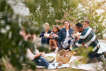 Glückliche Familie und Freunde beim Essen am Seeufer im Park - MASF11555