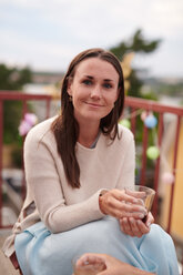 Porträt einer lächelnden jungen Frau mit einem Getränk in der Hand während einer Party auf einer Terrasse - MASF11568