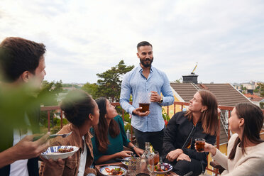 Mann unterhält sich mit Freunden auf einer Terrasse mit einem Getränk in der Hand - MASF11573