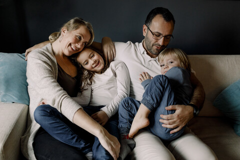 Glückliche, liebevolle Familie, die zusammen auf der Couch zu Hause sitzt, lizenzfreies Stockfoto