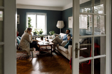 Familie, die verschiedene Technologien im Wohnzimmer verwendet, gesehen durch die Türöffnung zu Hause - MASF11590