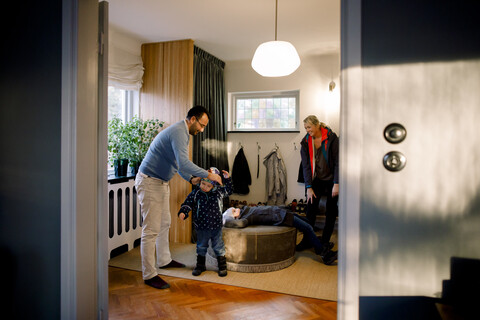 Vater, der seiner Tochter beim Anziehen hilft, gesehen durch eine Türöffnung zu Hause, lizenzfreies Stockfoto