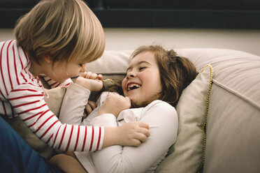 Verspieltes Mädchen kitzelt fröhliche Schwester auf der Couch zu Hause - MASF11595