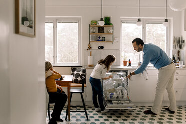 Father and daughter arranging utensils in dishwasher while standing at kitchen - MASF11604