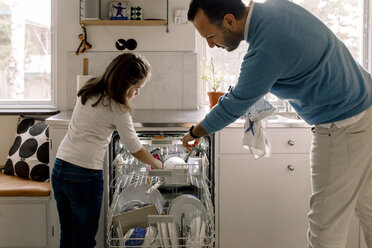 Father and daughter arranging utensils in dishwasher at kitchen - MASF11606