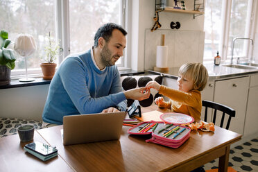 Daughter giving orange slice to father in kitchen at home - MASF11609