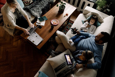 Hochformatige Ansicht einer Familie, die verschiedene Technologien im heimischen Wohnzimmer nutzt - MASF11615