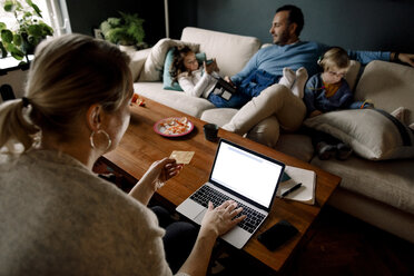 Mutter beim Online-Shopping, während Mann und Töchter im Wohnzimmer verschiedene Technologien nutzen - MASF11616