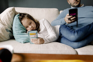 Father and daughter using mobile phones on couch at home - MASF11618