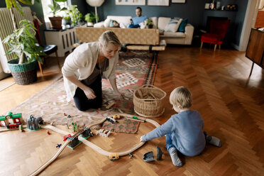 Mother looking at daughter playing with train set in living room - MASF11619