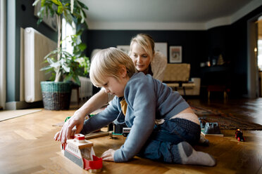 Mother and daughter playing with toy train on hardwood floor in living room at home - MASF11622