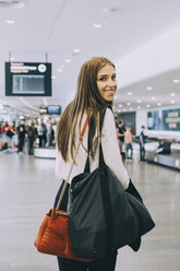 Porträt einer lächelnden jungen Geschäftsfrau, die mit Kollegen am Flughafen spazieren geht - MASF11632