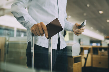 Mittelteil eines Geschäftsmannes, der am Flughafen seinen Reisepass und sein Smartphone hält - MASF11652