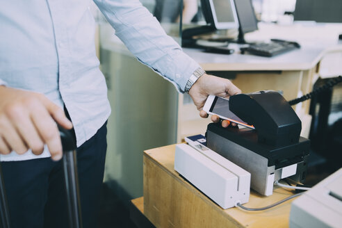 Mittelteil eines Geschäftsmannes, der am Check-in-Schalter eines Flughafens ein Ticket mit seinem Smartphone scannt - MASF11653