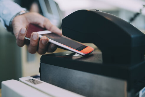Abgeschnittene Hände eines Geschäftsmannes, der ein Ticket mit seinem Smartphone am Flughafen-Check-in-Schalter scannt - MASF11655