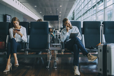 Thoughtful businessman looking away while sitting by female colleague at waiting area in airport - MASF11660