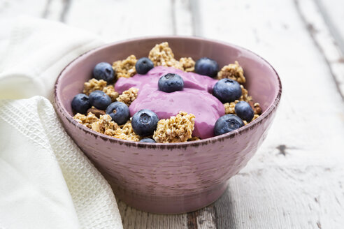 Granola with blueberries and blueberry yoghurt in bowl on white wood - LVF07884