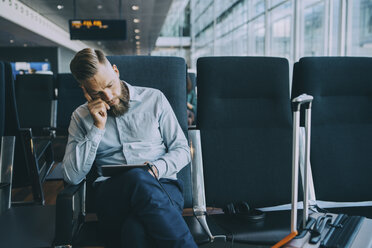 Geschäftsmann, der ein digitales Tablet benutzt, während er im Warteraum im Abflugbereich eines Flughafens sitzt - MASF11664