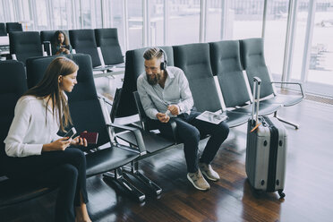 Lächelnder Geschäftsmann im Gespräch mit Geschäftsfrau beim Sitzen im Wartezimmer im Flughafen - MASF11666