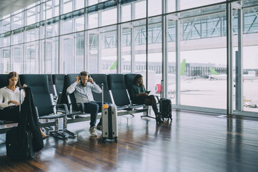 Full length of multi-ethnic colleagues waiting while sitting at airport departure area - MASF11668