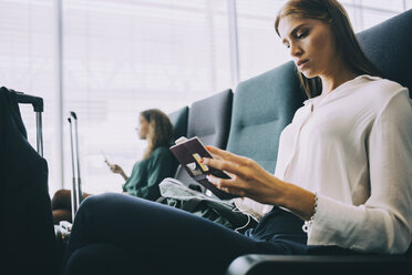 Young businesswoman looking at passport while sitting in airport departure area - MASF11669