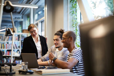 Männlicher Unternehmer lächelt, während er einer Bankmanagerin am Schreibtisch in einem kreativen Büro etwas erklärt - MASF11708