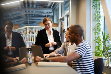 Männliche Unternehmer halten eine Präsentation für eine weibliche Bankmanagerin über einem Laptop am Schreibtisch in einem kreativen Büro - MASF11709