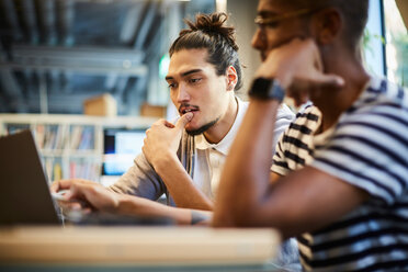 Männliche Unternehmer diskutieren über einem Laptop am Schreibtisch in einem kreativen Büro - MASF11715