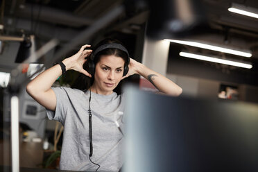 Kreative Geschäftsfrau mit Kopfhörern, die auf einen Computerbildschirm im Büro schaut - MASF11726