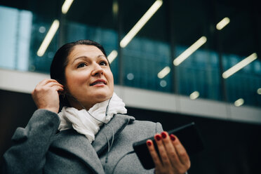 Low angle view of smiling businesswoman listening music while standing against building in city - MASF11746