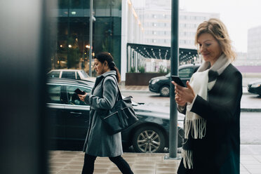 Geschäftsfrauen benutzen Smartphones beim Gehen auf dem Bürgersteig in der Stadt - MASF11749