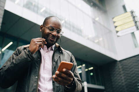 Low angle view of smiling businessman using smart phone while standing against building in city stock photo