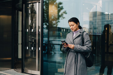 Geschäftsfrau, die ein Smartphone benutzt, während sie an einem Gebäude in der Stadt steht - MASF11764