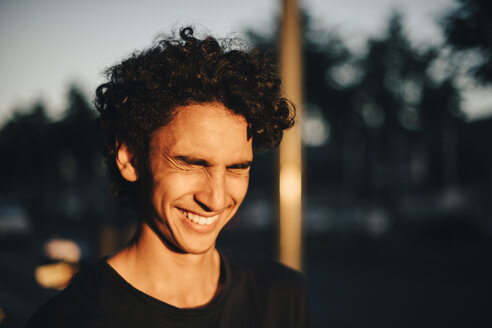 Cheerful teenage boy with eyes closed in city during sunset - MASF11767