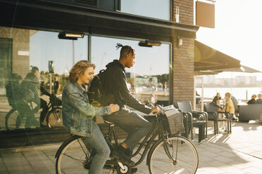 Teenage boy riding bicycle with cheerful friend in city during sunny day - MASF11801