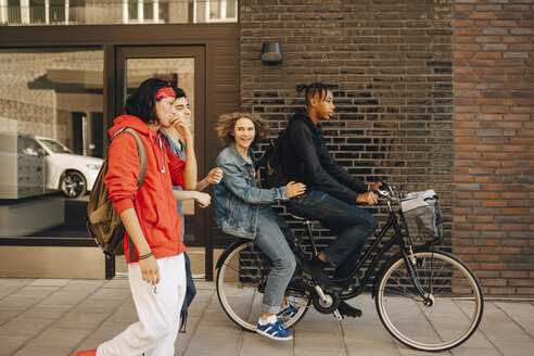 Fröhlicher junger Mann, der seine Freunde ansieht, während er mit dem Fahrrad durch die Stadt fährt - MASF11802